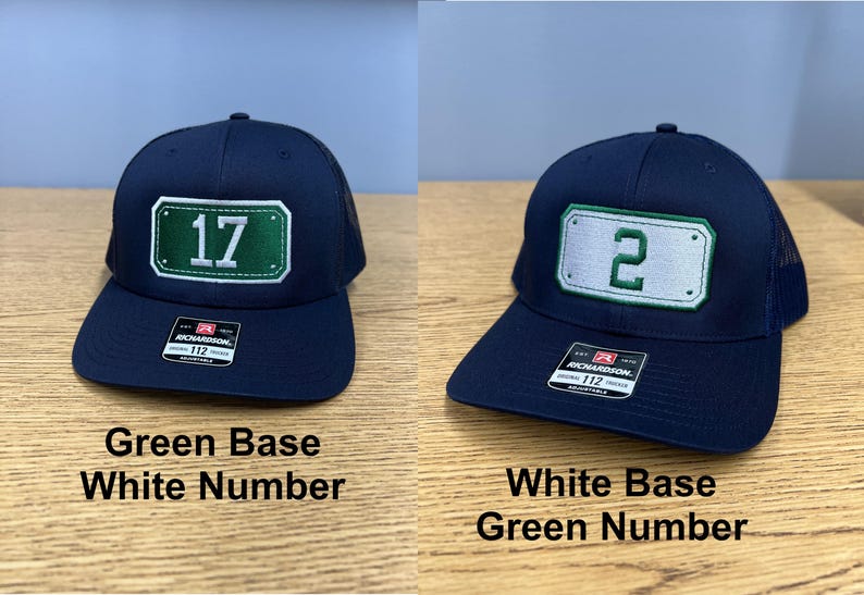 May include: Two navy blue baseball caps with mesh backs and adjustable snapback closures. One cap features a green rectangular patch with the white number 17, while the other displays a white rectangular patch with the green number 2. Both have stickers.
