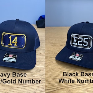 May include: Two adjustable trucker hats with mesh backs. The left hat is navy blue with a rectangular patch featuring the yellow number 14. The right hat is black with a rectangular patch featuring the white text E25. Both have Richardson labels.