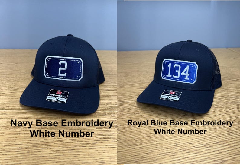 May include: Two baseball caps with mesh backs and adjustable straps. The left cap is navy blue with a white embroidered number 2 on a navy patch. The right cap is navy blue with a white embroidered number 134 on a royal blue patch. Both have stickers.