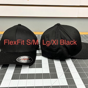 May include: Two solid black baseball caps with a structured crown and curved brim. The left cap features a silver and black sticker on the brim with the text FlexFit S/M. Red text overlay reads FlexFit S/M and Lg/Xl Black above the respective caps.