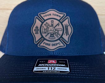 May include: A navy blue trucker hat with a brown leather patch featuring a firefighter's emblem. The patch has the text "Your Town Fire Dept." and depicts a firefighter's helmet, axe, ladder, hose, and fire hydrant. The hat has a black mesh back and a white adjustable strap with the text "Richardson 112 Original Trucker Adjustable" and the company logo.