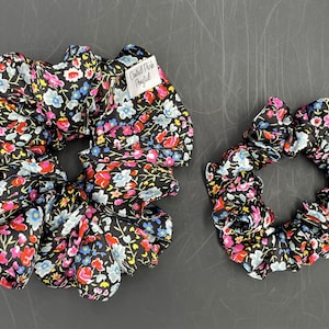 May include: Two black scrunchies with a floral print in pink, blue, and yellow. The scrunchies have a white label that says "Oxford Park Mayfield".