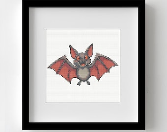 May include: Framed cross-stitch art featuring a pixelated bat with red wings and a gray body. The bat has an angry expression with red eyes and is set against a white background. The artwork is displayed in a black frame.