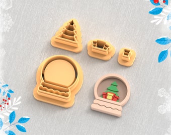 May include: A collection of clay cutters for earrings, including a Christmas tree, a house, and a snow globe design. The image also includes a snow globe with a Christmas tree and presents inside. The text at the top says "Clay Cutter for Earring". The text at the bottom says "STL FILE FOR 3D PRINTER".
