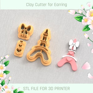 以下が含まれることがあります： 弓、ハート、エッフェル塔のデザインが施された、イヤリング用の粘土カッター3点セット。カッターは薄い茶色のプラスチック製で、ポリマークレイの使用を目的としています。表面には「STL FILE FOR 3D PRINTER」という文字が印刷されています。