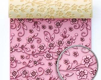Op de afbeelding: Een roze bloemenpatroon met een deegroller met een bijpassend reliëf bloemmotief. De deegroller heeft een lichtbeige kleur. De woorden "STL DIGITAL FILE" zijn gedrukt op een lichtblauwe rechthoek.