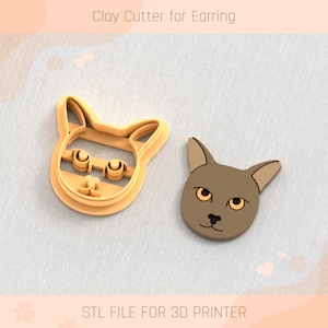 May include: A light orange clay cutter in the shape of a cat's head next to a brown cat head. The text "Clay Cutter for Earring" and "STL FILE FOR 3D PRINTER" are displayed above and below the objects.