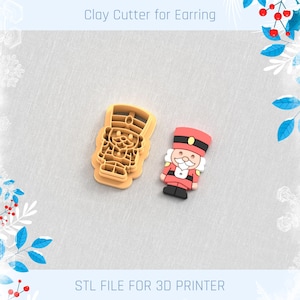 May include: A clay cutter and a finished earring shaped like a toy soldier. The cutter is light orange, and the earring is red, black, and white. The text "Clay Cutter for Earring" and "STL FILE FOR 3D PRINTER" are visible.