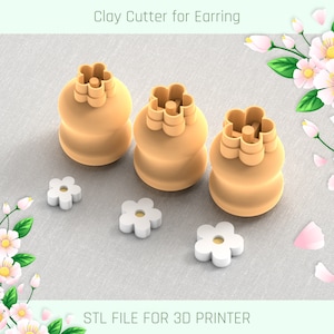 Könnte beinhalten: Drei 3D-gedruckte Ton-Ausstecher in Form von Blumen. Die Ausstecher sind in verschiedenen Größen und aus hellbraunem Kunststoff gefertigt. Die Ausstecher liegen auf einer hellgrauen Stoffoberfläche. Auf der Oberfläche befinden sich außerdem drei kleinere weiße Blumenformen. Der Text "STL FILE FOR 3D PRINTER" befindet sich am unteren Rand des Bildes.