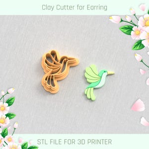 May include: A clay cutter and a finished earring in the shape of a hummingbird. The cutter is a light orange color, and the earring is green, light green, and yellow. The text "Clay Cutter for Earring" and "STL FILE FOR 3D PRINTER" are visible.