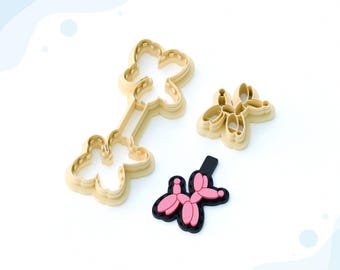 May include: Three 3D printed clay cutters for making balloon animal earrings. The cutters are beige and feature a balloon animal design. The cutters are on a white surface. STL FILE FOR 3D PRINTER.