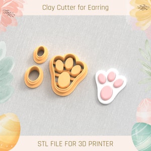 May include: Three clay cutters for making earrings. The cutters are shaped like a paw print, a circle, and a smaller circle. The paw print cutter is orange, and the circles are beige. The text "STL FILE FOR 3D PRINTER" is at the bottom of the image.