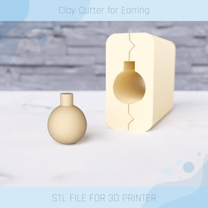 Op de afbeelding: Een 3D-geprinte kleiafsnijder voor het maken van ronde oorbellen. De snijder is beige en heeft een rond gat in het midden. De afbeelding toont ook een kleine, ronde, beige oorbel die met de snijder is gemaakt. "STL-BESTAND VOOR 3D-PRINTER" staat onderaan de afbeelding.