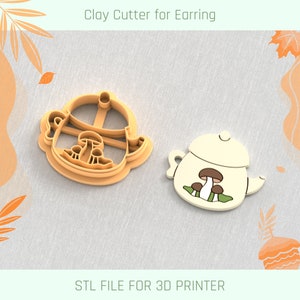 Può includere: Un tagliapasta in argilla stampato in 3D per orecchini a forma di teiera con funghi. Il tagliapasta è arancione e la teiera è bianca con funghi marroni e foglie verdi.