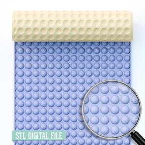 May include: A light blue surface with a repeating pattern of small, raised circles. A beige roller with a similar pattern rests on top. The words "STL DIGITAL FILE" are printed on a green rectangle at the bottom. A magnifying glass is in the foreground.