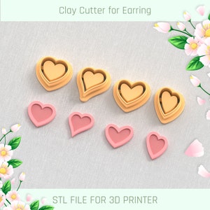 Puede incluir: Siete cortadores de arcilla en forma de corazón, tres son más grandes y de color naranja, cuatro son más pequeños y de color rosa. Los cortadores están dispuestos sobre una superficie rosa claro.  STL FILE FOR 3D PRINTER.