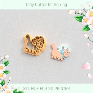 Könnte beinhalten: Zwei Ton-Ohrringausstecher. Einer ist eine hellorangefarbene Umrisslinie eines Truthahns mit floralen Details. Der andere ist eine hellorangefarbene Katze mit blauem Schal und weißen Blumen. Der Text oben lautet "Clay Cutter for Earring".