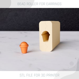 Op de afbeelding: Een 3D-geprinte kralenroller voor oorbellen. De roller is beige en heeft een kleine, ronde, oranje kraal erin. De tekst "STL FILE FOR 3D PRINTER" staat onderaan de afbeelding.