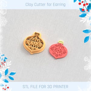 以下が含まれることがあります： クリスマスオーナメント型のベージュ色の粘土カッターと赤い粘土のイヤリング。カッターには詳細な花の模様があります。「Clay Cutter for Earring」と「STL FILE FOR 3D PRINTER」の文字が見えます。