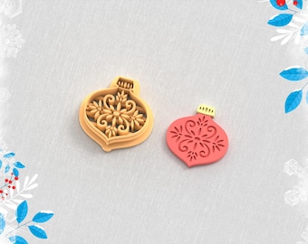 May include: A tan clay cutter and a red clay earring in the shape of a Christmas ornament. The cutter has a detailed floral design. The text "Clay Cutter for Earring" and "STL FILE FOR 3D PRINTER" are visible.
