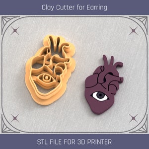 May include: A 3D printed clay cutter for earrings in the shape of a heart with an eye. The cutter is beige and the heart is purple. The text "STL FILE FOR 3D PRINTER" is at the bottom of the image.