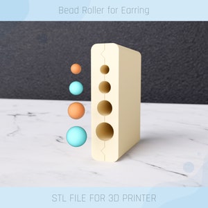 Può includere: Uno strumento di rotolamento per perline in plastica beige per realizzare orecchini. Lo strumento ha cinque fori di diverse dimensioni e l'immagine mostra quattro perline di diverse dimensioni e colori: arancione, blu e due tonalità di turchese.