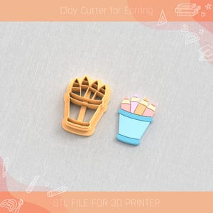 Può includere: Un tagliapasta in argilla e un orecchino finito a forma di portapenne. Il tagliapasta è arancione chiaro e l'orecchino è blu con matite rosa, arancioni e gialle. Il testo "Clay Cutter for Earring" e "STL FILE FOR 3D PRINTER" è visibile.