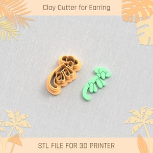 May include: Two 3D printed clay cutters for earrings. One cutter is orange and the other is green. The cutters are shaped like a stylized scorpion.