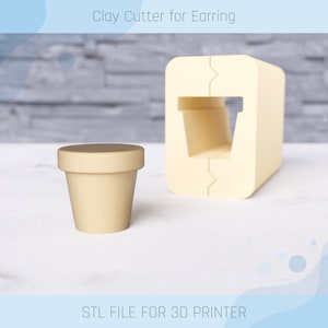 Peut inclure: Un emporte-pièce en argile imprimé en 3D pour boucles d'oreilles. L'emporte-pièce est beige et de forme rectangulaire avec une découpe au milieu. L'emporte-pièce est conçu pour créer une petite forme ronde pour les boucles d'oreilles. Le texte "Clay Cutter for Earring" est visible en haut de l'image. Le texte "STL FILE FOR 3D PRINTER" est visible en bas de l'image.