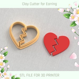 Könnte beinhalten: Ein 3D-gedruckter Ton-Ausstecher in Form eines gebrochenen Herzens. Der Ausstecher ist zum Herstellen von Ohrringen gedacht. Das Bild zeigt den Ausstecher neben einem roten Tonherz.