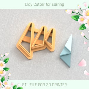 May include: A set of three triangle-shaped clay cutters for earrings. The cutters are made of a light brown plastic and are designed to be used with a 3D printer. The image also shows a small blue triangle-shaped object, which is likely a sample of the finished product.