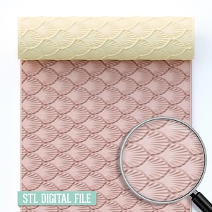 Puede incluir: Un rodillo con un patrón de conchas marinas, apoyado sobre una superficie rosa a juego. El rodillo es de color crema claro. El texto "STL DIGITAL FILE" está en la parte inferior. Una lupa está en la esquina inferior derecha.