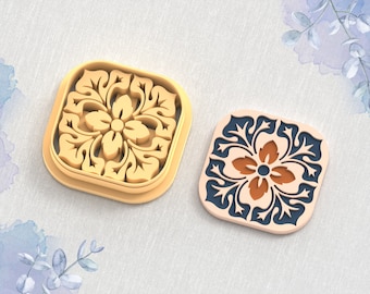 May include: Two 3D printed clay cutters for earrings, one in gold and one in blue and orange. The cutters are shaped like a square with a floral design in the center. The text "STL FILE FOR 3D PRINTER" is at the bottom of the image.