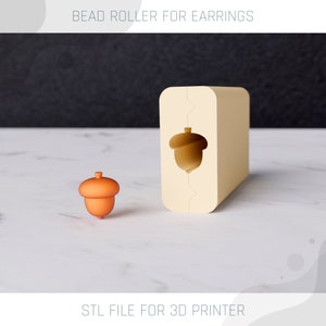 Könnte beinhalten: Ein 3D-gedruckter Perlenroller für Ohrringe in Form einer Eichel. Der Roller ist beige und die Eichel ist orange. Der Text "STL FILE FOR 3D PRINTER" befindet sich am unteren Rand des Bildes.