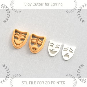 May include: Two 3D printed clay cutters shaped like theater masks. One mask is smiling and the other is frowning. The cutters are orange and white.