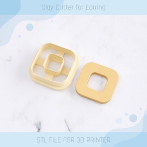 May include: A 3D printed clay cutter for earrings, in the shape of a square with a smaller square cut out in the center. The cutter is beige and the cut out is a lighter beige. The cutter is shown on a white marble surface. STL FILE FOR 3D PRINTER