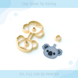 May include: A 3D printed clay cutter for earrings in the shape of a koala. The cutter is beige and has a detailed design. The image also shows a sample earring made with the cutter, which is gray with black eyes and nose.