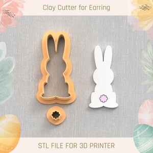 May include: A 3D printed clay cutter for earrings in the shape of a bunny rabbit. The cutter is made of white plastic and has a pink flower on the back. The cutter is designed to be used with polymer clay to create bunny rabbit earrings.
