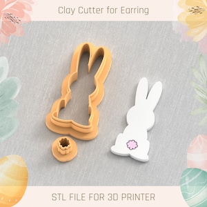 May include: A 3D printed clay cutter for earrings in the shape of a bunny. The cutter is brown and has a small, round, pink detail on the bunny's tail. The cutter is on a white fabric background. STL FILE FOR 3D PRINTER.