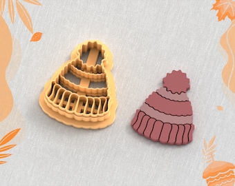 May include: A clay cutter for earrings in the shape of a winter hat, next to a finished earring. The cutter is light orange, and the earring is shades of pink and red. The text "Clay Cutter for Earring" and "STL FILE FOR 3D PRINTER" are at the top and bottom.
