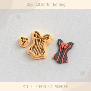 May include: A 3D printed clay cutter for earrings, shaped like a corset with a bow. The cutter is orange and the bow is red. The image also shows a smaller cutter shaped like a bow.