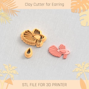 May include: A 3D printed clay cutter for earrings, shaped like a betta fish. The cutter is made of orange plastic and has a detailed design. The image also shows a separate cutter for the fish's fin.