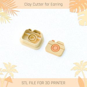 Puede incluir: Un cortador de arcilla para pendientes en forma de cámara, impreso en 3D. El cortador es beige con un detalle naranja claro. El texto "STL FILE FOR 3D PRINTER" está en la parte inferior de la imagen.