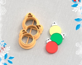 May include: A 3D printed clay cutter for making Christmas ornament earrings. The cutter is shaped like three stacked ornaments. There are three ornaments in the image, one red, one green, and one yellow.