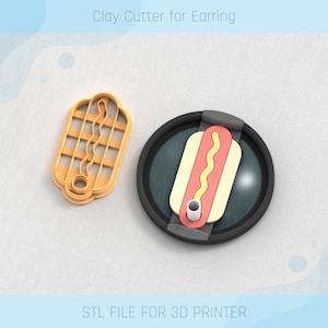 May include: A 3D printed clay cutter for earrings shaped like a hot dog. The cutter is orange and has a detailed design. The image also shows the cutter on a black base with a hot dog design.