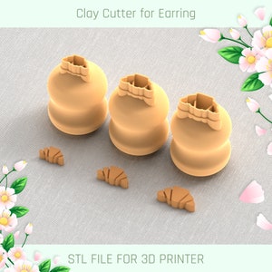 Puede incluir: Tres cortadores de arcilla color beige para pendientes, con forma de croissant, sobre una superficie gris claro. Los cortadores están acompañados de tres recortes más pequeños con forma de croissant. El texto "Clay Cutter for Earring" y "STL FILE FOR 3D PRINTER" son visibles.