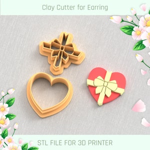Puede incluir: Dos cortadores de arcilla impresos en 3D para pendientes. Un cortador tiene forma de corazón y el otro es un lazo. Los cortadores están sobre un fondo de tela marrón claro. ARCHIVO STL PARA IMPRESORA 3D.