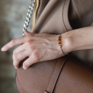 May include: A simple bracelet with a black cord and small amber beads. The bracelet is worn on a person's wrist.