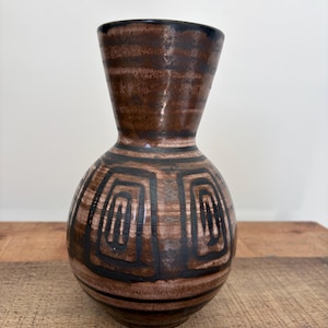May include: A ceramic vase with a bulbous body and a flared neck, featuring a brown and tan glazed finish. The surface is decorated with dark brown horizontal bands and a series of repeating, hand-painted black geometric spiral patterns.