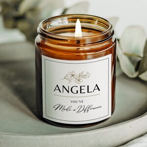 May include: A brown glass candle with a white label that reads "Angela You've Made a Difference". The label has a gold floral design and a dotted line.